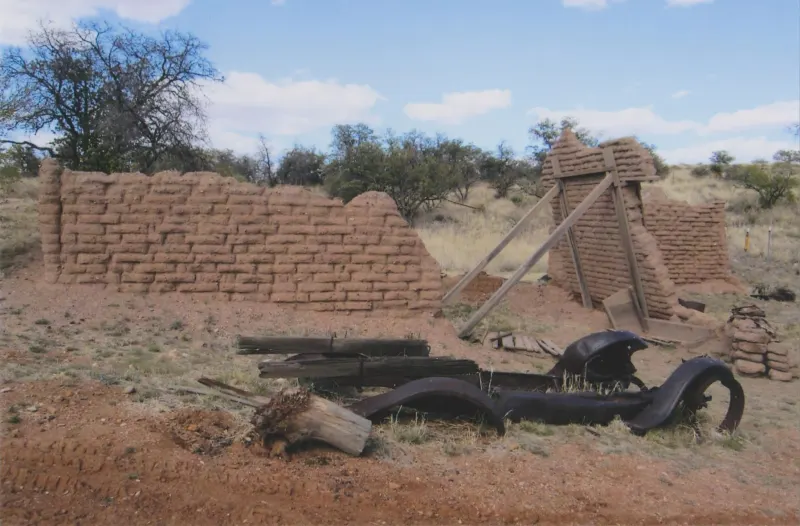 An abandoned early automobile and adobe walls on red earth